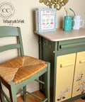 Cactus Silk All-In-One paint is perfect for painting kitchen cabinets, bathroom cabinets and painting furniture.
A kitchen cart paired with a chair both painted in Cactus Silk All-In-One Mineral Paint® with the doors painted from the Chalk Mineral Paint line in Rebel Yellow as well as the Belles and whistles Magnolia garden transfer on the doors and the top has Voodoo gel stain in Au naturel. Staged with two mason jar cups blue and white with metal straws and a "HOMEMADE RECIPES" cookbook.