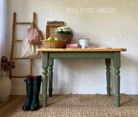 Cactus Silk All-In-One paint is perfect for painting kitchen cabinets, bathroom cabinets and painting furniture.
A table with its base and legs painted in Cactus Silk All-In-One paint with the top in a natural wood color. Staged with woven baskets and decor, books, flowers, A stick ladder with two cloth bags hanging on the ladder with a pair of black rain boots on the left side of the piece.