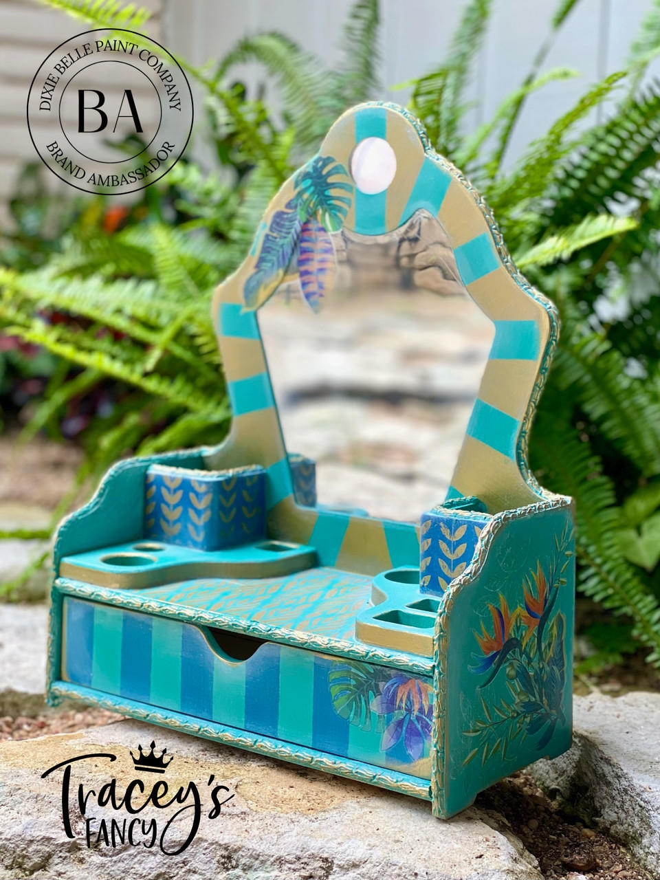 Cape Current Silk All-In-One paint is perfect for painting kitchen cabinets, bathroom cabinets and painting furniture.
Miniature vanity painted in Cape Current Silk All-In-One Mineral Paint® with gold stripes on the mirror and a darker blue stripes on the base. As well as Tropical Leaves - Transfer is seen on the side and top of the mirror. Staged outside with greenery behind the piece.