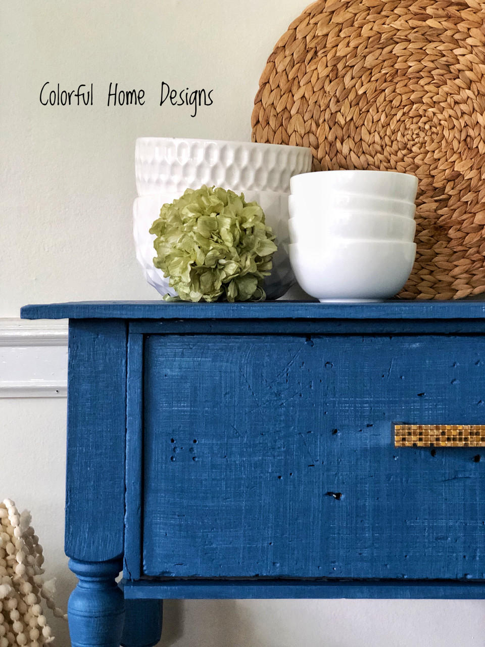 Cape Current Silk All-In-One paint is perfect for painting kitchen cabinets, bathroom cabinets and painting furniture.
Corner view of an entryway table painted in Cape Current Silk All-In-One paint with white bowls stacked on top of eachother staged on the table with green leaf ball.