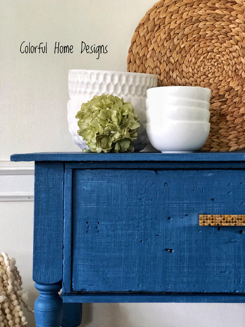 Cape Current Silk All-In-One paint is perfect for painting kitchen cabinets, bathroom cabinets and painting furniture.
Corner view of an entryway table painted in Cape Current Silk All-In-One paint with white bowls stacked on top of eachother staged on the table with green leaf ball.