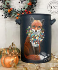 Silk All-In-One Mineral Paint Deep Sea Silk Paint.
There is a large clay bucket painted with Deep Sea Silk all-in-one mineral paint.  There is a painted fox on the front of the bucket with  flowered wreath around the fox's neck.  Next to the clay bucket there are two gourds with gold leaves that wrap around the table.  On the white wall behind is another wreath with dried berries and leaves.