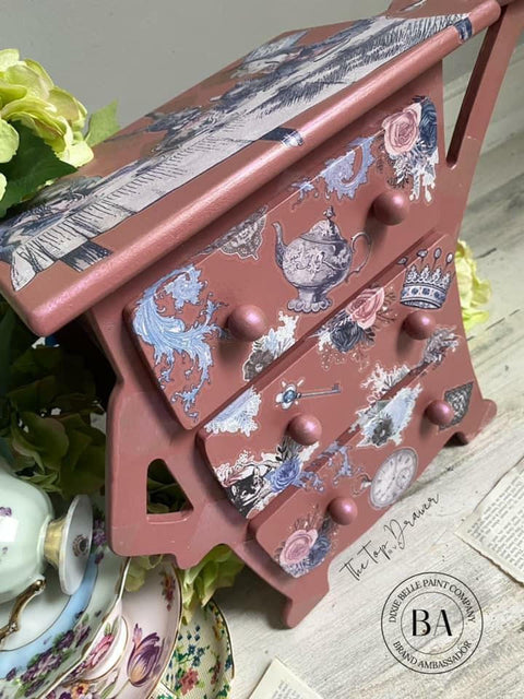 Desert Rose Silk All-In-One paint is perfect for painting kitchen cabinets, bathroom cabinets and painting furniture
This is an eclectic children's dresser is painted in Desert Rose CMP and has lots of Alice transfers.  On top is the big transfer of Alice and the rabbit sitting next to the big table.  There are china plates stacked to the left of the child's dresser with a china tea cup turned over on the top plate.  There are yellow flowers behind the china plates.