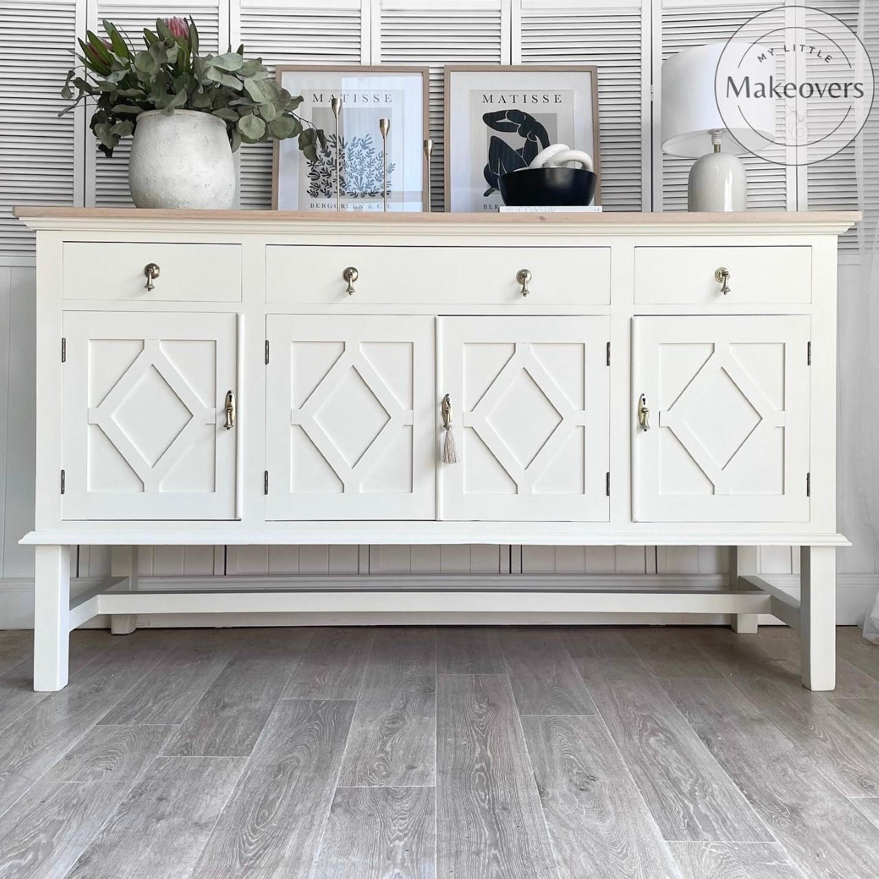Endless Shore Silk All-In-One paint is perfect for painting kitchen cabinets, bathroom cabinets and painting furniture. White painted buffet with bronze pulls and a light wood top. Large white vase containing faux greenery. Tan lamp with a white lampshade.