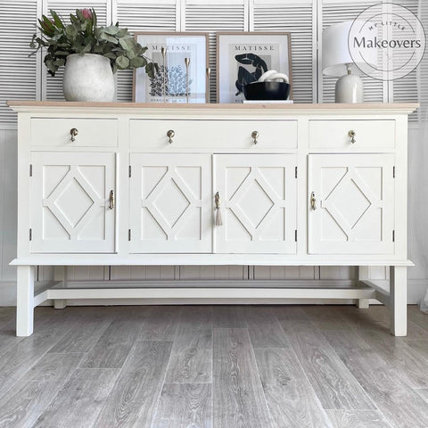 Endless Shore Silk All-In-One paint is perfect for painting kitchen cabinets, bathroom cabinets and painting furniture. White painted buffet with bronze pulls and a light wood top. Large white vase containing faux greenery. Tan lamp with a white lampshade.