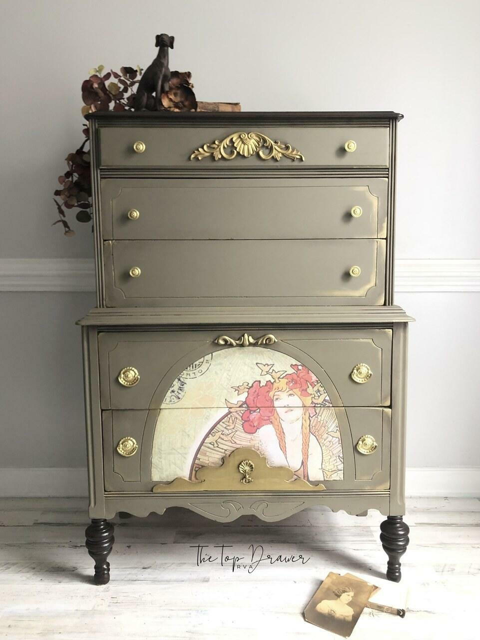 Hampton Olive Silk All-In-One paint is perfect for painting kitchen cabinets, bathroom cabinets and painting furniture.
A chest of drawers painted in Hampton Olive Silk All-In-One paint with gold hardware. A painting of a woman in a semicircle is seen on the bottom half of the piece.