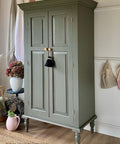 Hampton Olive Silk All-In-One paint is perfect for painting kitchen cabinets, bathroom cabinets and painting furniture.
A wardrobe painted in Hampton Olive Silk All-In-One paint, staged with flower vases and blankets hanging on the wall besides the piece.