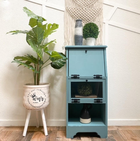 Harbor Silk All-In-One paint is perfect for painting kitchen cabinets, bathroom cabinets and painting furniture.
Secretary desk painted in Harbor Silk All-In-One paint with black hardware staged with potted houseplants around the piece on wood floors and white wall.