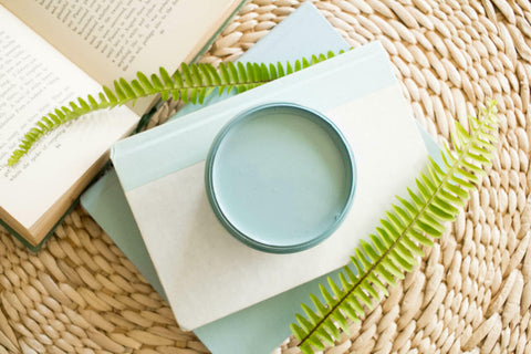 Harbor Silk All-In-One paint is perfect for painting kitchen cabinets, bathroom cabinets and painting furniture.
Top view of an opened container of the Harbor Silk All-In-One paint staged with white/blue books stack on eachother and an opened book on the side, staged on top of a woven rattan background.