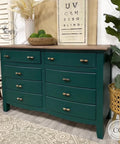 Midnight Green Silk All-In-One paint is perfect for painting kitchen cabinets, bathroom cabinets and painting furniture. Dark green Silk all in one painted dresser with wood stained top. Staged with a potted plant, a wood bowl with grass balls and a vase with wheat, also has a vision board wall décor on top.