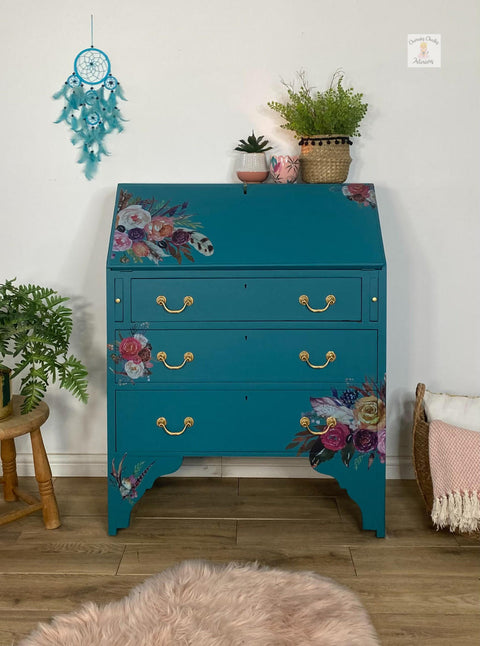 Mirage Silk All-In-One paint is perfect for painting kitchen cabinets, bathroom cabinets and painting furniture. Blue Green Silk All-In-One paint dresser with gold hardware and floral rub on transfers. staged with potted plants and a fuzzy rug with a dream catcher hanging on the wall.