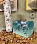 Mirage Silk All-In-One paint is perfect for painting kitchen cabinets, bathroom cabinets and painting furniture. Blue Green Silk All-In-One paint Ombre case with floral rub on transfers. Staged next to a tube of Belles and whistles Dewy Morning transfers, sitting on top of a wicker plate holder and wood beads wrapped around.
