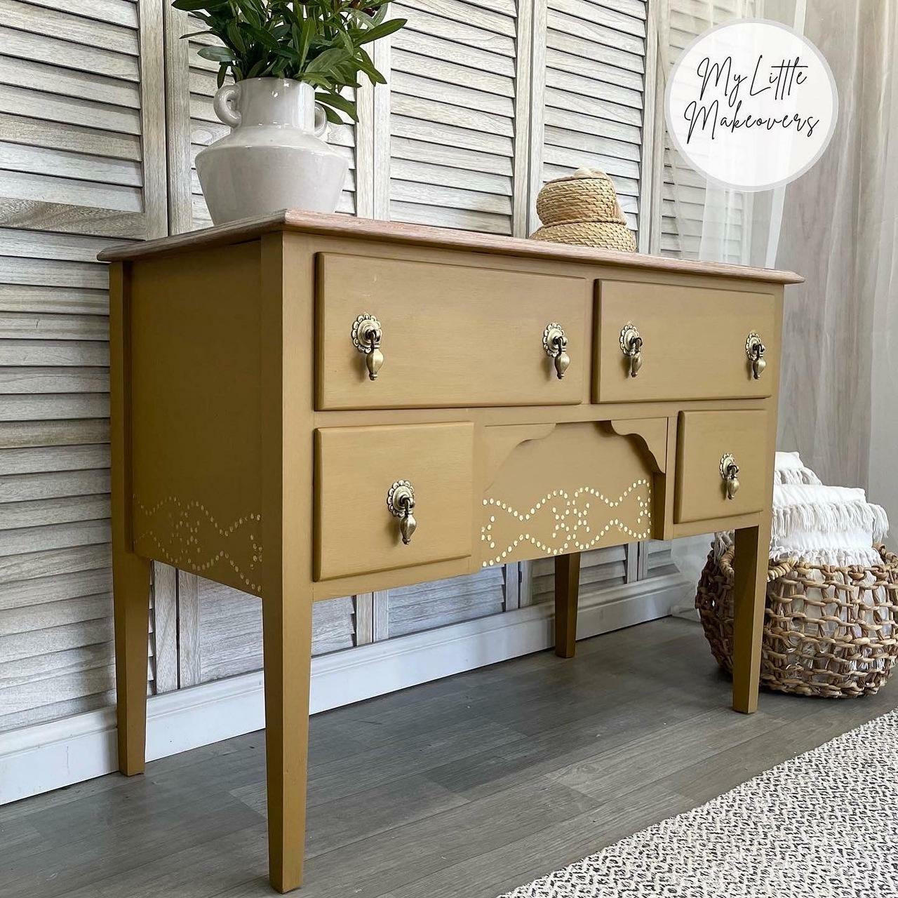 Mojave Silk All-In-One paint that is perfect for painting kitchen cabinets, bathroom cabinets and painting furniture. Dark Yellow desk with nailhead trim stencil for accent, and gold hardware. Staged with potted plant and a wicker basket.