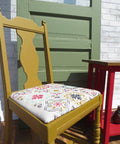 Mojave Silk All-In-One paint is perfect for painting kitchen cabinets, bathroom cabinets and painting furniture. Yellow Silk painted chair with a colorful fabric on top. Staged outside by a green door and red end table.