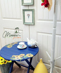 Nautical Silk All-In-One paint is perfect for painting kitchen cabinets, bathroom cabinets and painting furniture. Dark blue painted outdoor table with sunflower rub on transfer. Staged next to flowers, yellow vase and a tea set placed on top of the table.