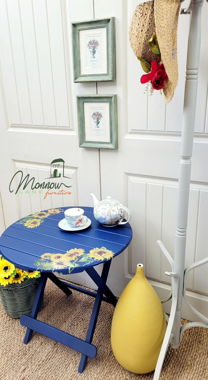 Nautical Silk All-In-One paint is perfect for painting kitchen cabinets, bathroom cabinets and painting furniture. Dark blue painted outdoor table with sunflower rub on transfer. Staged next to flowers, yellow vase and a tea set placed on top of the table.