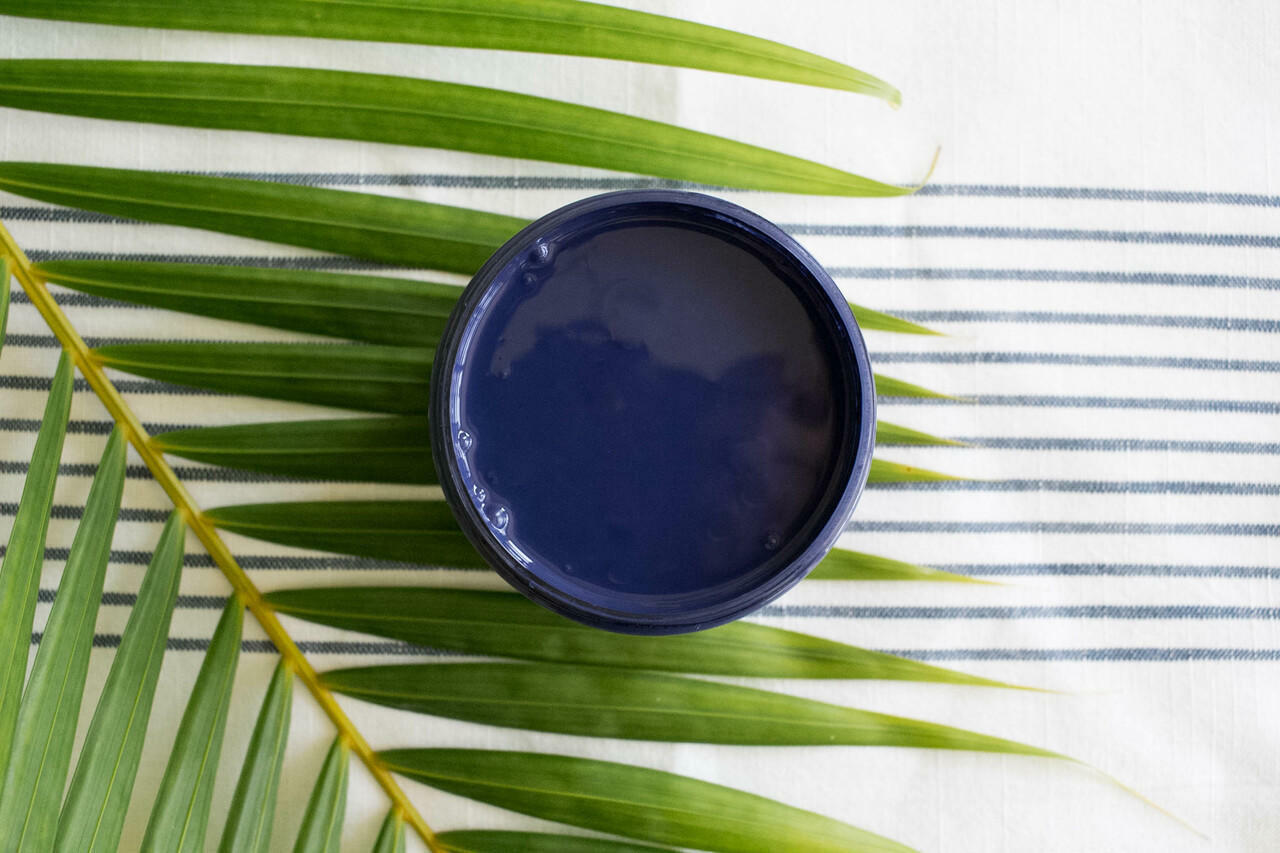 Nautical Silk All-In-One paint is perfect for painting kitchen cabinets, bathroom cabinets and painting furniture. Dark blue open paint can top view sitting on a palm frond.