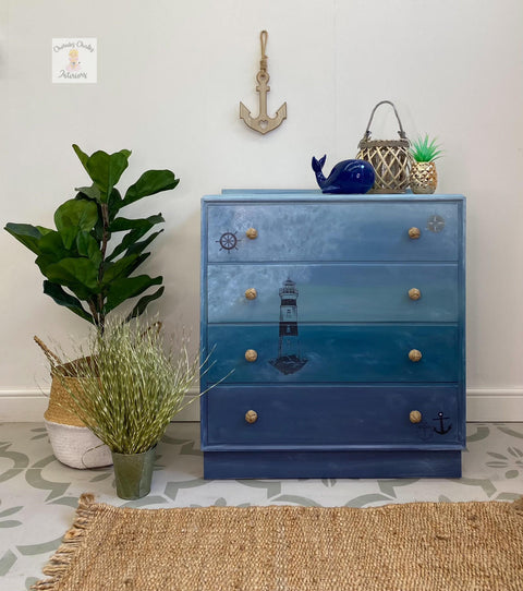 Nautical Silk All-In-One paint is perfect for painting kitchen cabinets, bathroom cabinets and painting furniture. light and dark blue Ombre dresser with wicker style hardware. Painted on nautical stencils on the drawers. Staged  with potted plants and a whale figure.