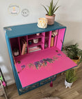 Oasis Silk All-In-One paint is perfect for painting kitchen cabinets, bathroom cabinets and painting furniture. Blue chalk painted secretary desk with pink chalk painted inside. Tropical leaves rub on transfer on the front and inside the desk. Staged with books, and candles and a plant.