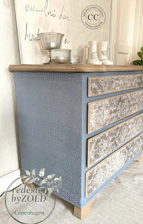 Quiet Cove Silk All-In-One paint is perfect for painting kitchen cabinets, bathroom cabinets and painting furniture! The front drawers and top of this 4 drawer dresser look distressed with a white stencil on top, whereas the base and sides are painted in this medium-gray paint with raised stenciling. This dresser is staged with glassware, a canvas with cursive, and little white decorative boots on top.