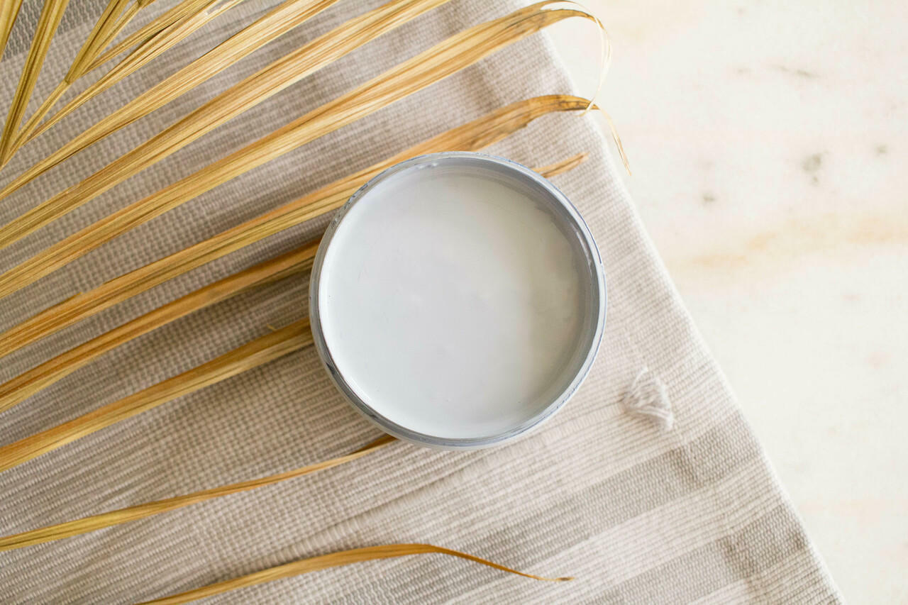 Quiet Cove Silk All-In-One paint is perfect for painting kitchen cabinets, bathroom cabinets and painting furniture! A top view of the medium blue-gray paint in an open jar staged with fabric and a dried palm leaf to the left of the open jar.