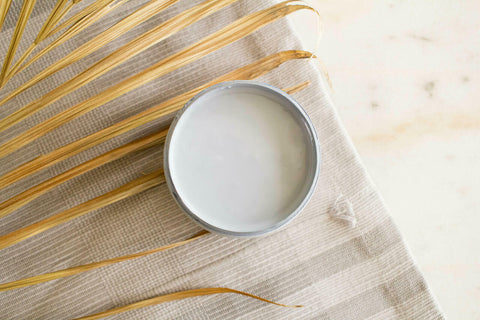 Quiet Cove Silk All-In-One paint is perfect for painting kitchen cabinets, bathroom cabinets and painting furniture! A top view of the medium blue-gray paint in an open jar staged with fabric and a dried palm leaf to the left of the open jar.