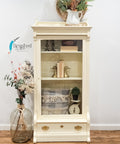 Sun Kissed Silk All-In-One paint is perfect for painting kitchen cabinets, bathroom cabinets and painting furniture.
Small display cabinet painted in Sun Kissed Silk All-In-One paint with one drawer at the bottom with gold hardware. Staged with niknaks, books and baskets inside the cabinet, besides piece is a large glass jug with flowers and branches.
