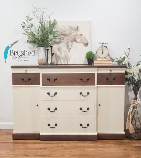 Sun Kissed Silk All-In-One paint is perfect for painting kitchen cabinets, bathroom cabinets and painting furniture.
A wide dresser with Sun Kissed Silk All-In-One Mineral Paint as the majority color and brown stained top drawers with a brown stained top and base. Stage with a horse canvas and some greenery in pots on top of dresser. In a room with wood laminated floor and white wall.