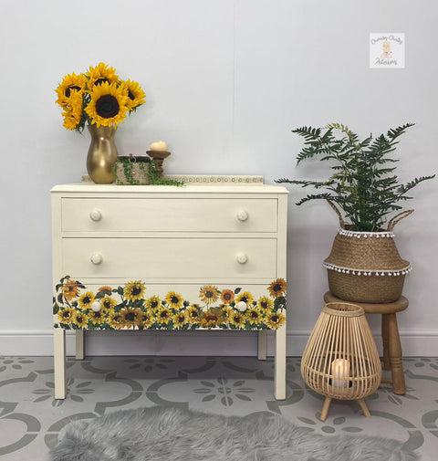 Sun Kissed Silk All-In-One paint is perfect for painting kitchen cabinets, bathroom cabinets and painting furniture.
Chest of drawers painted in Sun Kissed Silk All-In-One paint with the Sunflower transfer along the bottom last drawer. Staged with a metal vase with sunflower, greenery and woven baskets. In a gray patterned floor and white wall.