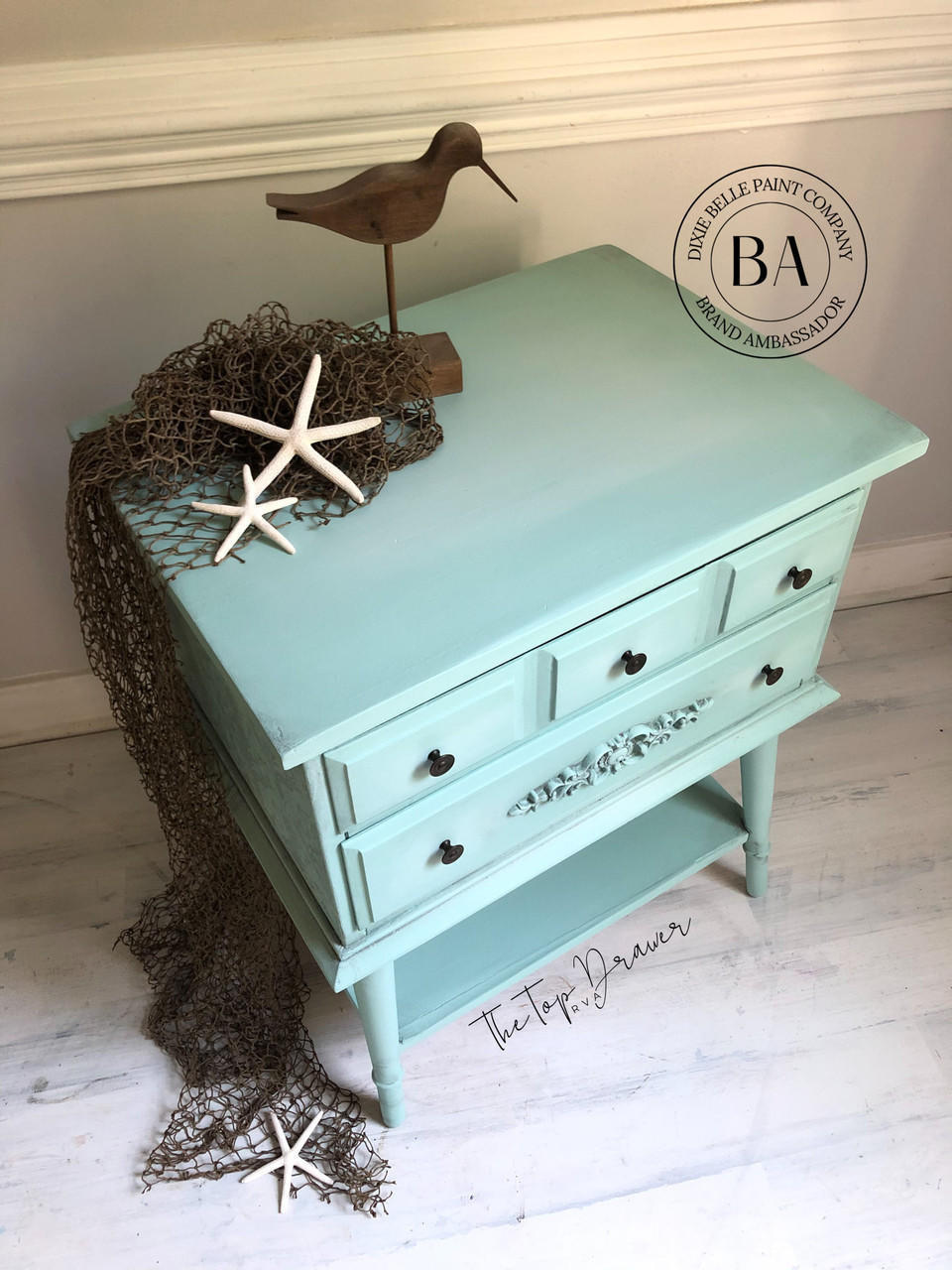 Tide Pool Silk All-In-One paint is perfect for painting kitchen cabinets, bathroom cabinets and painting furniture.  A blue chalk painted corner table with a wooden bird, star fish and a fishing net sitting on top and around; with black knobs.