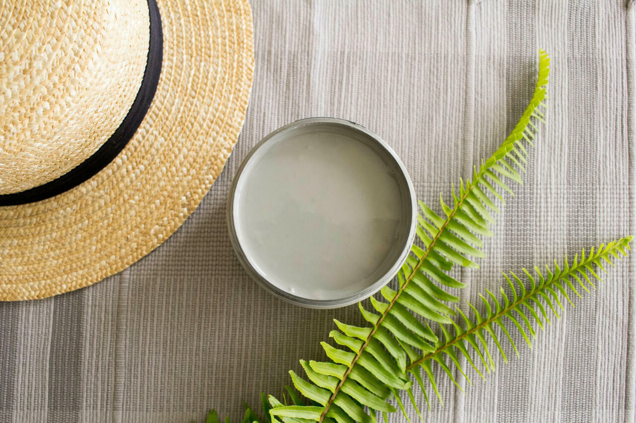 Wharf Silk All-In-One paint is perfect for painting kitchen cabinets, bathroom cabinets and painting furniture.  Top view of an open jar of Wharf Silk All-In-One paint sitting on a tan and brown piece of cloth.  A light brown woven hat with a black band sits to the left of the jar, and a two green fern branches are to the right of the jar.