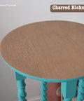 Round wooden table with a natural top and teal-painted twisted legs. "Sisterhood Furniture" and "Charred Hickory" are written on the image.