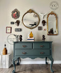 Bluish gray painted dresser makeover with bronze pulls. Staged with a stack of books with a yellow vase and a white sculpture of a hand doing a peace sign, with two bronze busts on top.