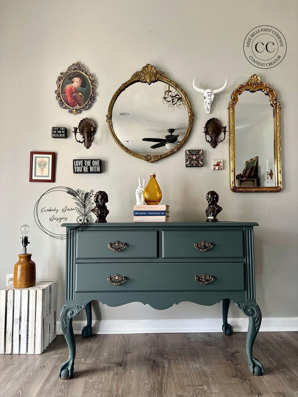 Bluish gray painted dresser makeover with bronze pulls. Staged with a stack of books with a yellow vase and a white sculpture of a hand doing a peace sign, with two bronze busts on top.
