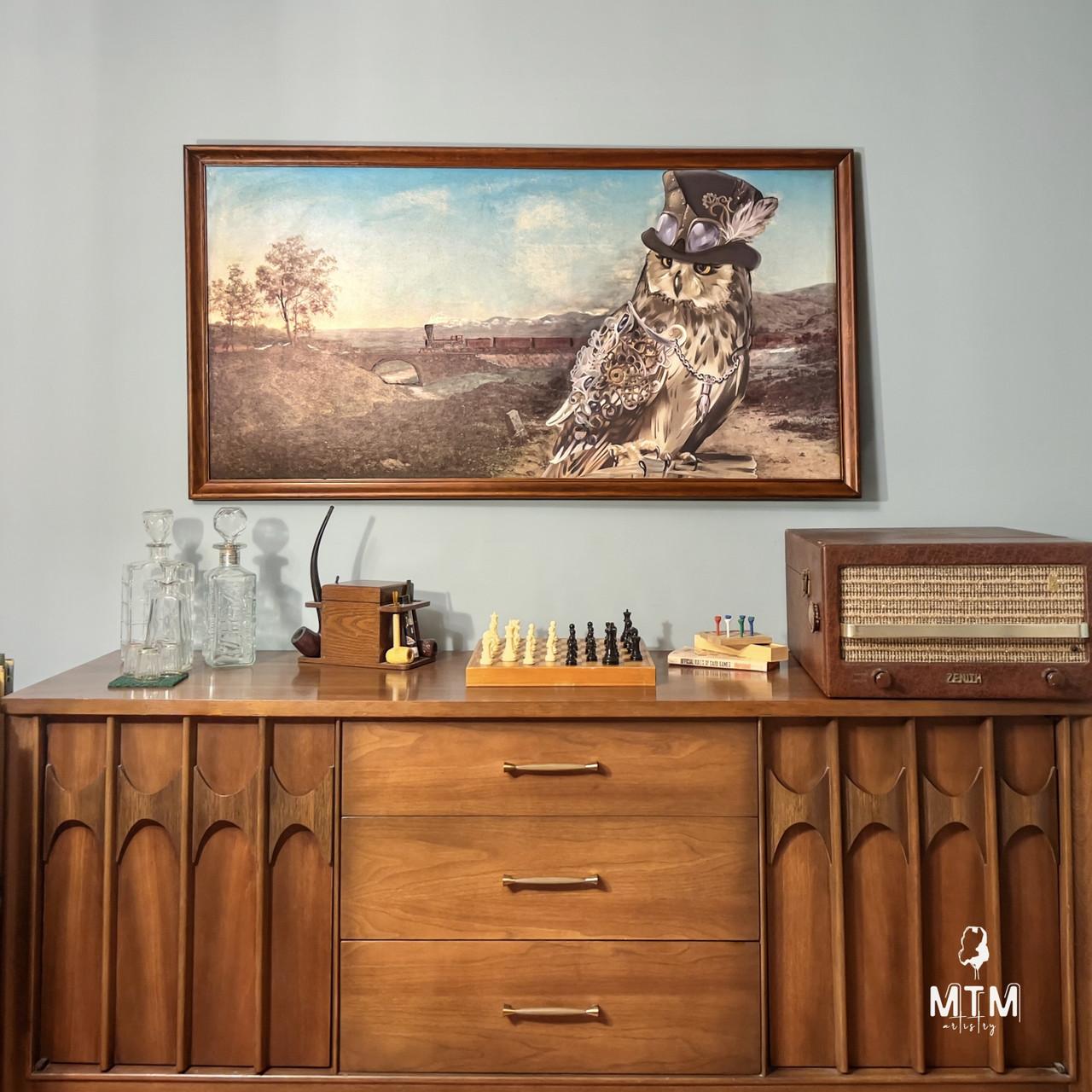 A mid-century modern wooden sideboard is adorned with various items: a set of crystal decanters, a small wooden box, a chess set, and a vintage radio. Above the sideboard, a framed painting features an owl wearing a hat and goggles in a scenic landscape.