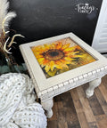 A vintage-style painted coffee table with an ornate Sunny Daze A1 Rice Decoupage Paper design on the tabletop, set against a dark wall with a cozy chunky knit blanket on the side.