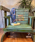 Rustic wooden porch swing type beach chair. The Surf's Up Decoupage Paper has been applied to the middle of the back of the chair and distressed. With a scarf draped over the back of the chair and a Hawaii book placed on the seat.