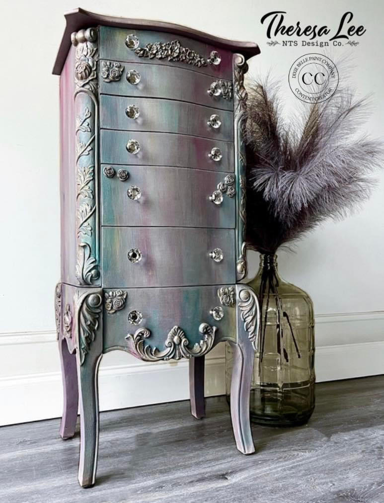 Bougainvillea Terra Clay Paint provides endless possibilities for your imagination and can be used on wood, canvas, tile, fabric and more!
Chest of drawers painted with Bougainvillea Terra Clay Paint and a blend of colors to give it a goth look. Staged with a large jug with feathers inside on gray wood floors in front of white wall.