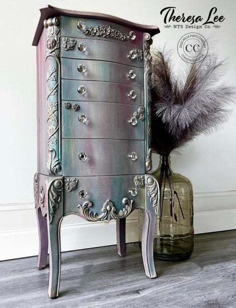 Bougainvillea Terra Clay Paint provides endless possibilities for your imagination and can be used on wood, canvas, tile, fabric and more!
Chest of drawers painted with Bougainvillea Terra Clay Paint and a blend of colors to give it a goth look. Staged with a large jug with feathers inside on gray wood floors in front of white wall.