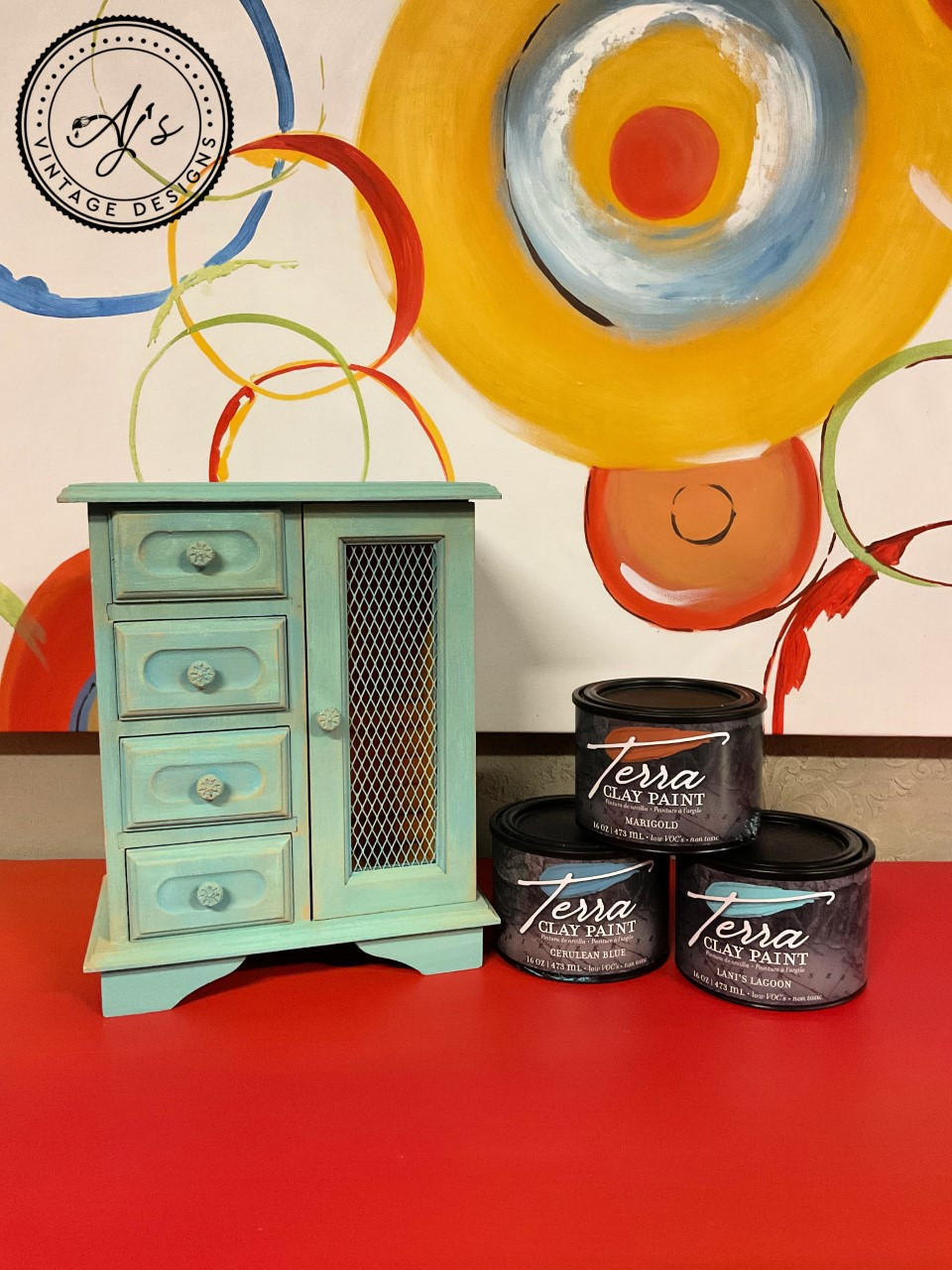 Cerulean Blue Terra Clay Paint provides endless possibilities for your imagination and can be used on wood, canvas, tile, fabric and more!
Jewelry box painted in Cerulean Blue Terra Clay Paint staged with containers of Cerulean Blue, Marigold, and Lani's Lagoon Terra Clay Paint Stacked ontop of eachother
