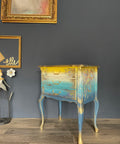 Cerulean Blue Terra Clay Paint provides endless possibilities for your imagination and can be used on wood, canvas, tile, fabric and more!
Bedside table with ombre design going from yellow to a tan fading into a Cerulean Blue Terra Clay Paint blending in to  Blue Moon Terra Clay Paint. Using gold hardware and gold on woodwork. Staged In front of black wall and gold picture frames.