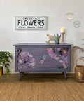 Elderberry Terra Clay Paint provides endless possibilities for your imagination and can be used on wood, canvas, tile, fabric and more! Purple clay painted chest with legs, Translucent Garden rub on furniture Transfer applied on the front of the chest. Large metal "Fresh Cut Flowers, Stems, Blooms, Seeds" sign on the wall over the piece. Metal vase with lavender flowers, and a beige candlestick on top.