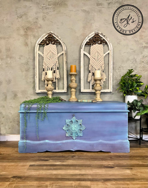 Lani's Lagoon Terra Clay Paint provides endless possibilities for your imagination and can be used on wood, canvas, tile, fabric and more!
A chest painted with a blend of Elderberry, Blue Moon, Lani’s Lagoon, and Daffodil all from the Terra Clay Paint line , with the WoodUBend Applique #1323.26 is seen in the center of the pieces painted with Lani's Lagoon Terra Clay Paint. Staged with candle pedestal and greenery.