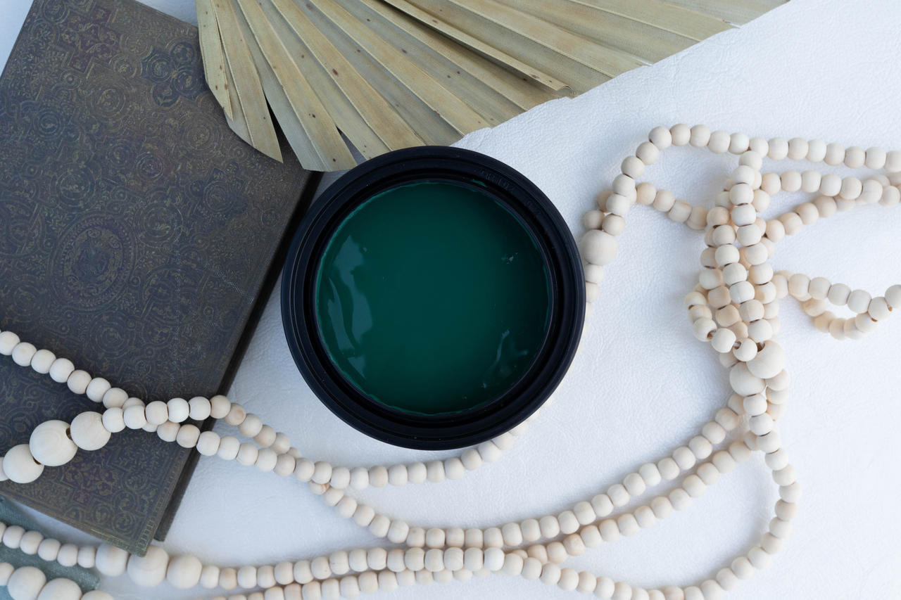 Malachite Terra Clay Paint provides endless possibilities for your imagination and can be used on wood, canvas, tile, fabric and more!
Open container of Malachite Terra Clay Paint staged with white wooden beads, a black book and Large dry leaf around container.