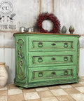 Malachite Terra Clay Paint provides endless possibilities for your imagination and can be used on wood, canvas, tile, fabric and more!
French Baroque dresser with black hardware painted in Malachite Terra Clay Paint using the Patina green on the bottom half giving it a rusty vibe. Staged with a red berry wreath and silver metal decor on top of piece.