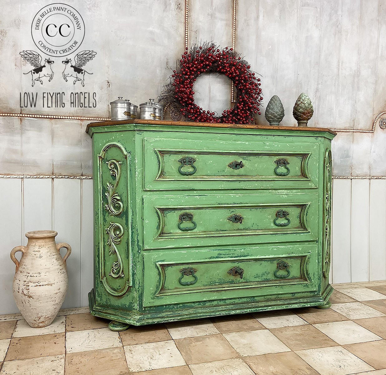 Malachite Terra Clay Paint provides endless possibilities for your imagination and can be used on wood, canvas, tile, fabric and more!
French Baroque dresser with black hardware painted in Malachite Terra Clay Paint using the Patina green on the bottom half giving it a rusty vibe. Staged with a red berry wreath and silver metal decor on top of piece.