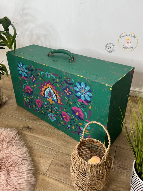 Malachite Terra Clay Paint provides endless possibilities for your imagination and can be used on wood, canvas, tile, fabric and more!
Wooden suitcase with handle facing up painted in Malachite Terra Clay Paint with distressed edges and corners, the Latin Floral Transfer is seen on the front side.