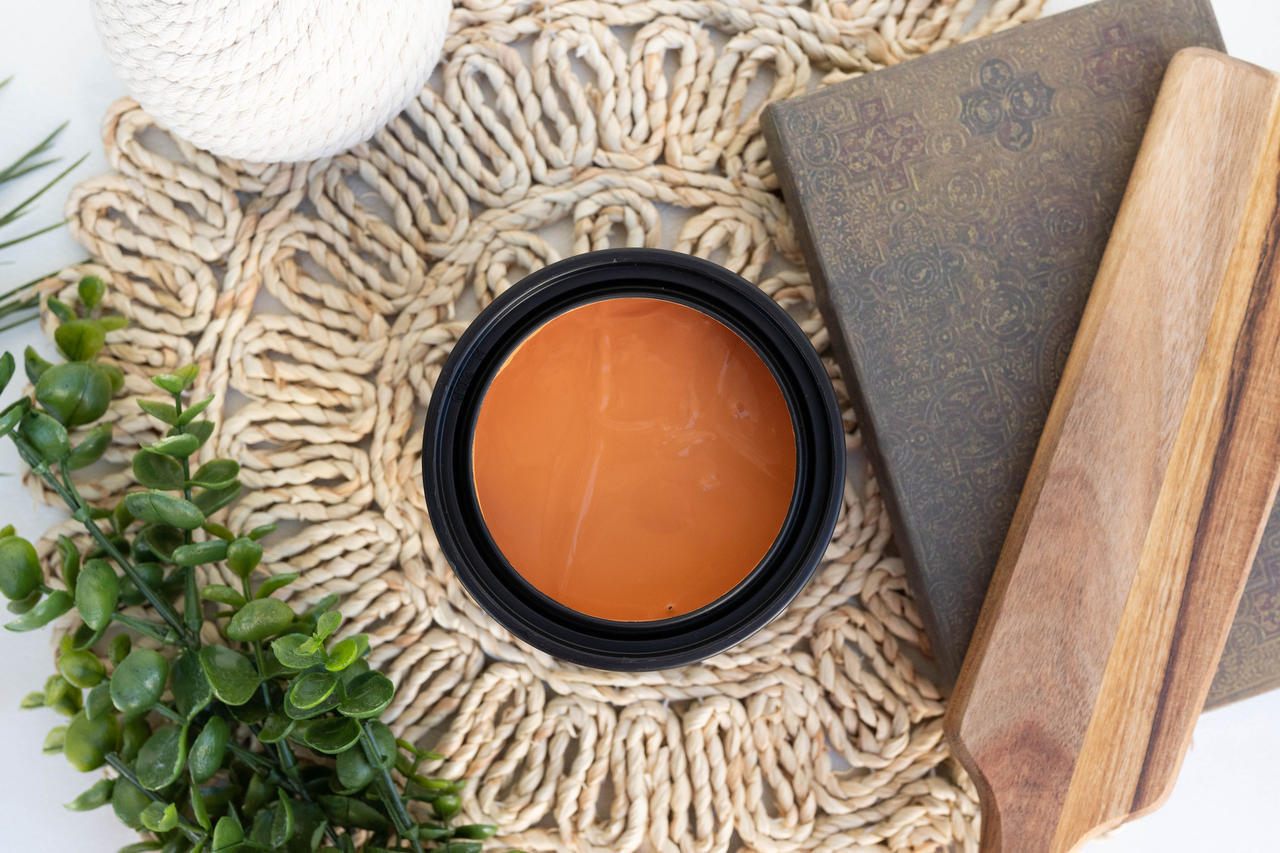 Marigold Terra Clay Paint provides endless possibilities for your imagination and can be used on wood, canvas, tile, fabric and more! Orange can of Terra Clay artisan paint sitting on a wicker table cover with a book, wood cutting board, and ivy plant around it.