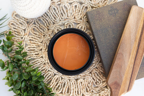 Marigold Terra Clay Paint provides endless possibilities for your imagination and can be used on wood, canvas, tile, fabric and more! Orange can of Terra Clay artisan paint sitting on a wicker table cover with a book, wood cutting board, and ivy plant around it.