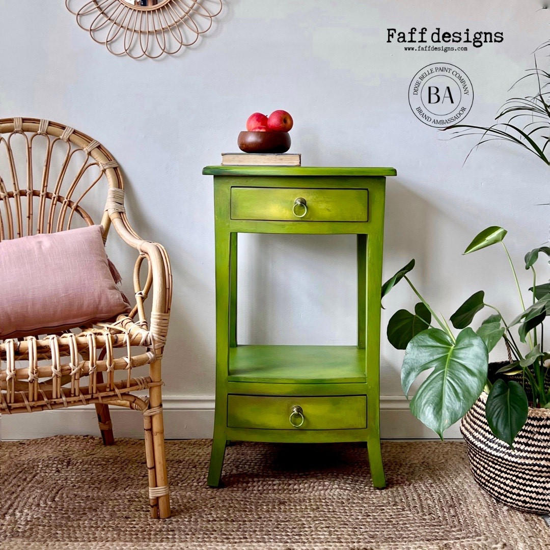 Pistachio Terra Clay Paint provides endless possibilities for your imagination and can be used on wood, canvas, tile, fabric and more! Light green clay painted end table blended with yellow clay paint. Staged with a bowl of apples and a plant also has a wicker chair next to it.